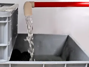 Water flowing from a red pipe into a gray container with black objects inside, likely for aquarium setup.