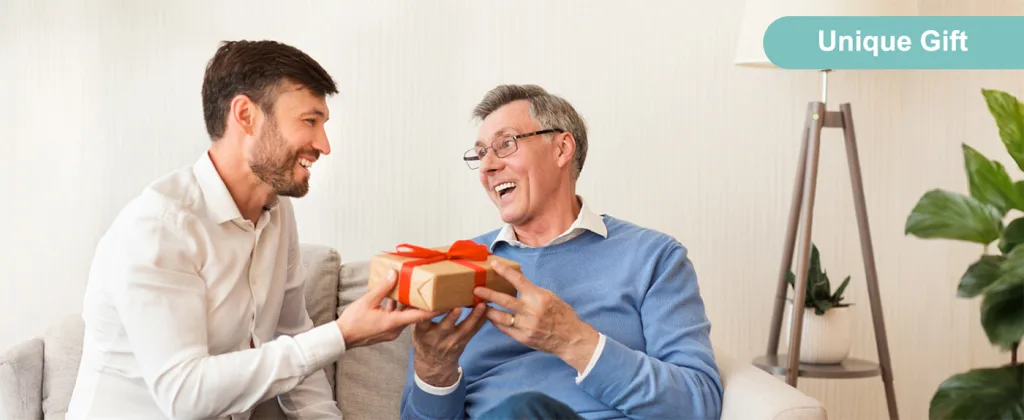 A young man presents a unique gift box to an older man, both smiling warmly in a cozy living room setting.