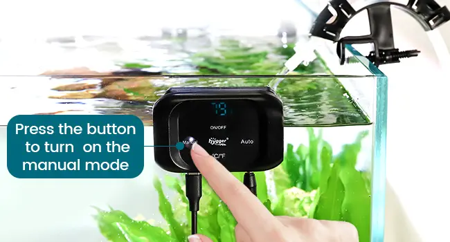 Hand pressing button on Hygger aquarium controller to activate manual mode with water flow visible in tank