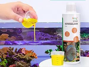 Hand pouring yellow liquid into aquarium with Aqua Balance water treatment bottle and colorful fish visible